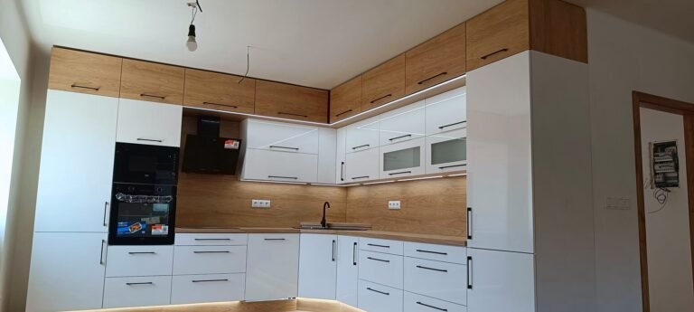Bílá rohová kuchyně s dubovými horními skříňkami a LED podsvícením